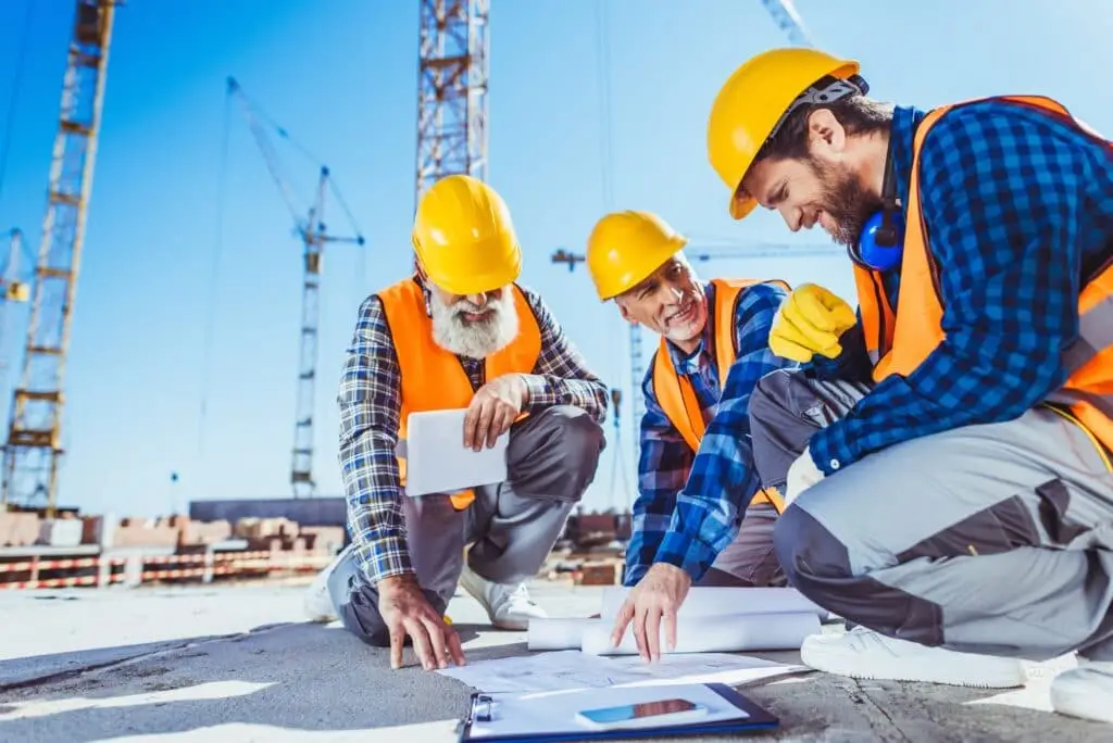 Three construction workers sitting on concrete at construction site, discussing building plans