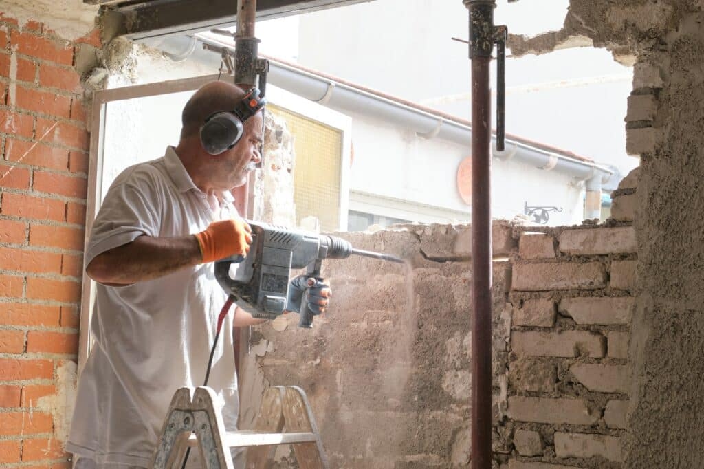 Mason breaking a house wall with a demolition hammer.