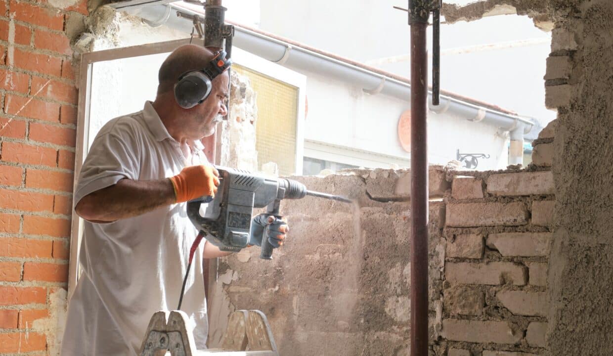 Mason breaking a house wall with a demolition hammer.